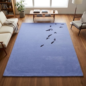 May include: A rectangular area rug in a solid periwinkle blue color featuring a flock of dark navy blue birds flying in a diagonal pattern across the surface. The rug has a soft, plush texture and is positioned flat on a wooden floor.