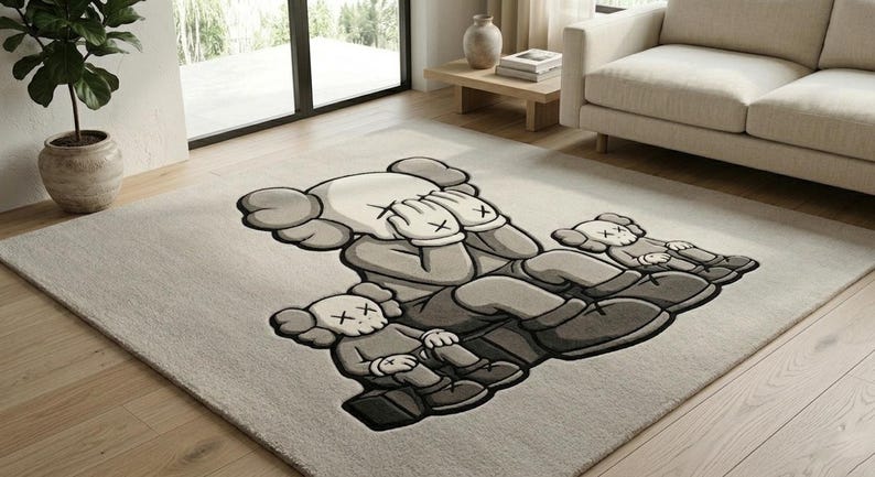 A luxurious hand tufted wool area rug displayed in a bright modern living room with hardwood floors. The rug features a large streetwear-style cartoon bear character holding two smaller companion figures, rendered in warm cream, medium grey, and deep charcoal tones. The plush wool pile creates rich texture and depth. Soft natural light highlights the dimensional design. A beige sofa and indoor plant complete the minimalist, hype-culture-inspired interior setting.