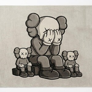 K&ouml;nnte beinhalten: Grau-wei&szlig;er Teppich mit einer Cartoonfigur, die sich die Augen verdeckt, flankiert von zwei kleineren Figuren. Die Figuren haben X-f&ouml;rmige Augen und sitzen. Der Teppich hat einen neutralen Hintergrund.
