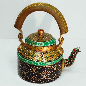 Op de afbeelding: Een handbeschilderde theepot met een houten handvat en tuit. De theepot heeft gedetailleerde patronen in goud, groen, rood en wit op een zwarte basis. Het handvat is van hout en de tuit is versierd met rode en groene accenten.