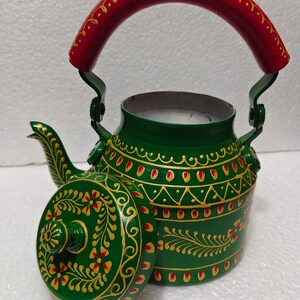 May include: A green metal teapot featuring a red handle and a matching removable lid. The exterior is decorated with hand-painted gold and red floral and geometric patterns. The teapot has a curved spout and a sturdy metal handle attached to the top.