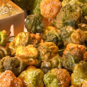 Könnte beinhalten: Nahaufnahme eines Haufens bunter, holpriger Paprika. Die Paprika reichen in der Farbe von Grün bis Orange und Gelb und haben eine strukturierte, unebene Oberfläche. Die Paprika sind eng beieinander, was eine lebendige und appetitliche Darstellung ergibt.