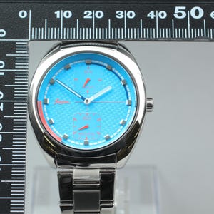 May include: A stainless steel wristwatch with a light blue face and silver hands. The watch has a textured dial and a silver band. The watch face measures approximately 1.5 inches in diameter.