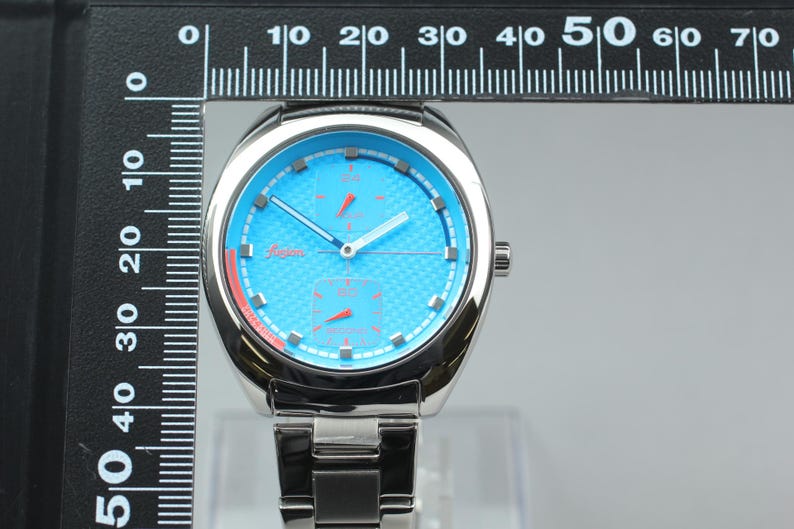 May include: A stainless steel wristwatch with a light blue face and silver hands. The watch has a textured dial and a silver band. The watch face measures approximately 1.5 inches in diameter.
