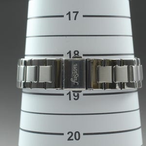May include: A silver-toned watch band with a clasp that reads "Fusion" is displayed on a white measuring cone. The watch band is made of rectangular links. The cone has black horizontal lines and numbers.