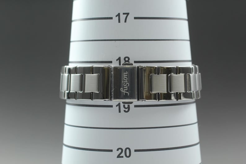 May include: A silver-toned watch band with a clasp that reads "Fusion" is displayed on a white measuring cone. The watch band is made of rectangular links. The cone has black horizontal lines and numbers.