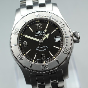 Puede incluir: Reloj automático ORIS plateado con esfera negra. El reloj tiene agujas e indicadores luminosos, visualización de fecha y bisel giratorio. Resistente al agua hasta 200 metros y con correa de acero inoxidable.
