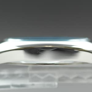 May include: Side view of a silver wristwatch with a light blue face. The watch has a curved, polished metal case and a matching metal band. The watch is displayed against a blurred background.
