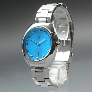 May include: A silver-toned wristwatch with a vibrant blue face and red accents. The watch features a stainless steel band and a unique, modern design. The watch is displayed on a clear stand.