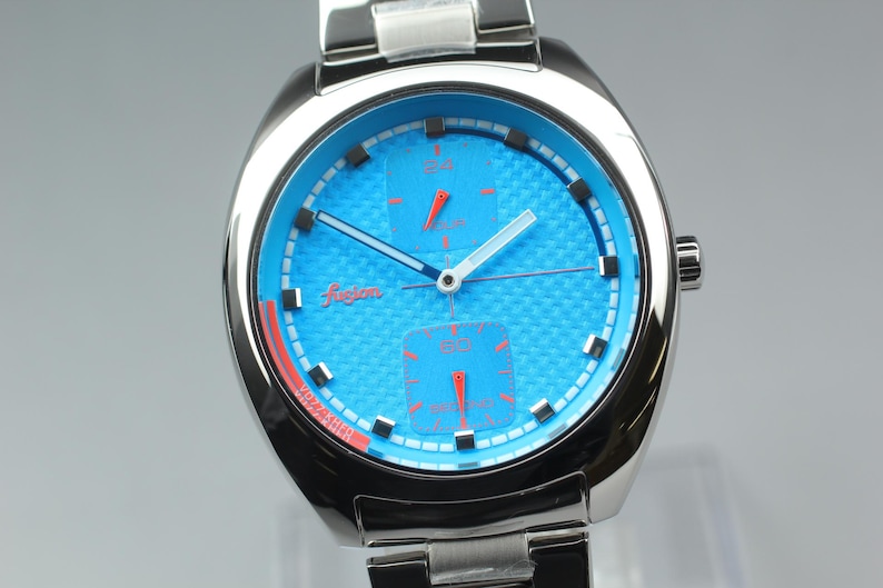 May include: A stainless steel wristwatch with a vibrant blue face and a textured pattern. The watch features red accents, including the hands and the word "fusion" in a cursive font. The watch has a silver band and a round face.