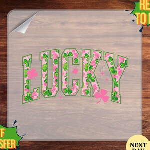May include: A DTF transfer with the word "LUCKY" in a green and pink floral design with shamrocks. The transfer is on a clear sheet with the words "READY TO PRESS" and "DTF TRANSFER".