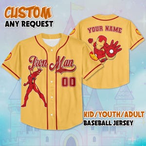 May include: A yellow baseball jersey with red trim, featuring the words "Iron Man" and the number "00". The front displays an Iron Man graphic. The back has an Iron Man graphic and the words "YOUR NAME". The jersey is available for kids, youth, and adults.