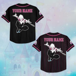 May include: Black baseball jersey with pink trim and the text "YOUR NAME" on the back. Features a cartoon illustration of a superhero. The jersey has short sleeves and a button-up front. A second jersey with a pinstripe design is also visible.