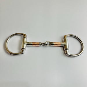 May include: A stainless steel D-ring horse bit with copper accents. The bit features a D-shaped ring on each side, connected by a copper and stainless steel mouthpiece. This equestrian equipment is designed for controlling a horse.