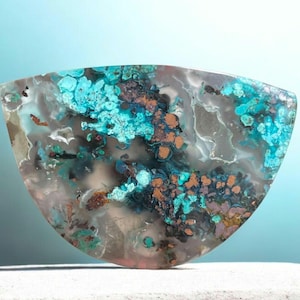 May include: A polished gemstone with a unique, organic pattern. The stone features a mix of colors, including turquoise, brown, and gray, creating a striking visual effect. The shape is a rounded, irregular form, adding to its natural appeal.