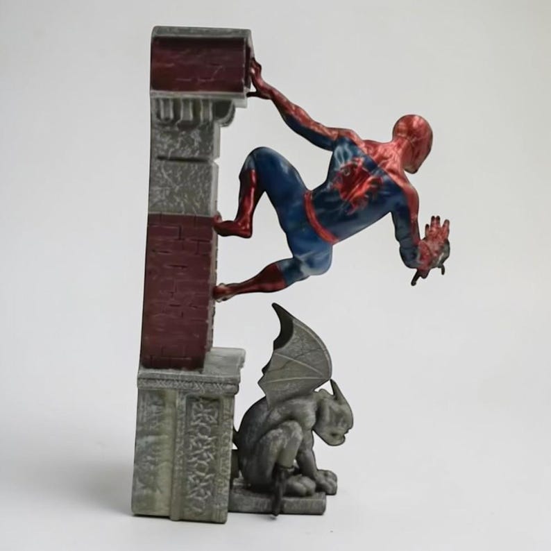 Puede incluir: Una figura de Spider-Man en una pose din&aacute;mica, trepando por una estructura de ladrillo y piedra. La figura lleva un traje cl&aacute;sico rojo y azul. Una estatua de g&aacute;rgola est&aacute; debajo. La estructura tiene un aspecto envejecido.