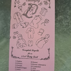 May include: A pink card with a black and white illustration of a baby doll layette pattern. The card includes a list of 14 items for a 1-7/8 inch baby doll, including a nightie, kimono, romper, bonnet, and undershirt.