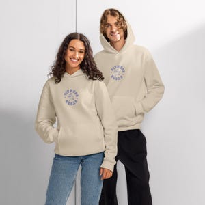 May include: Two people wearing matching beige hoodies with a front pocket and a hood. Each hoodie has a circular blue and white graphic that reads "Fitness Store". The person on the left is wearing blue jeans, and the person on the right is wearing black pants.