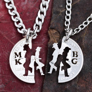May include: Two silver necklaces with matching pendants. The pendants are cut out of silver coins and feature a couple holding hands. The coins are engraved with the initials "MK" and "BG".