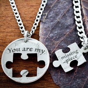 May include: Two silver necklaces with a puzzle piece design. One necklace has a coin with the words "You are my" and a puzzle piece cut out. The other necklace has a puzzle piece with the words "missing piece" engraved on it.