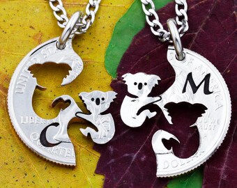 Puede incluir: Dos collares de plata con colgantes de koala, cada colgante es la mitad de un koala entero, los colgantes están hechos de una moneda de 25 centavos de dólar estadounidense, un colgante tiene la letra "M".