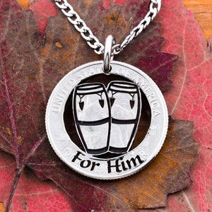 May include: Silver necklace with a half dollar coin pendant featuring a cutout design of two conga drums. The coin has the words "United States of America" and "For Him" inscribed on it.