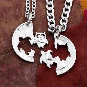 May include: Two silver necklaces with owl charms. The charms are made from cut-out silver dollar coins. The owl charms are connected to form a heart shape.