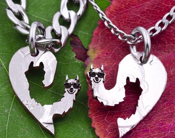 Puede incluir: Dos collares de plata con colgantes en forma de corazón que representan una silueta de llama. La llama lleva gafas de sol y un pequeño corazón en el pecho. Los collares están sobre un fondo de hoja verde y hoja roja.