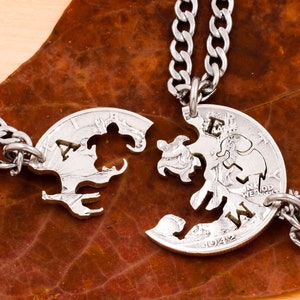 May include: Two silver-colored, half-circle pendant necklaces, each with a chain, are displayed on a brown leaf. The pendants, cut from coins, fit together like puzzle pieces. One pendant has the letters "A" and "W" cut out, and the other has the letter "E".