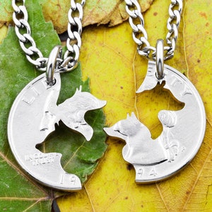 May include: Two silver necklaces with matching pendants. Each pendant is a silver coin with a cutout design of two foxes facing each other. The foxes are kissing and the coins are connected to form a heart shape.