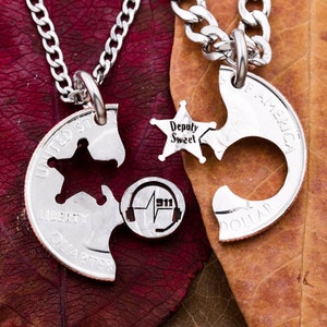 May include: Two silver necklaces with matching coin pendants. The pendants are cut out in the shape of a star and a crescent moon. The star pendant has the words "Deputy Sweet" engraved on it. The crescent moon pendant has the words "United States of America" and "Liberty" engraved on it. The necklaces are on a brown and red background.
