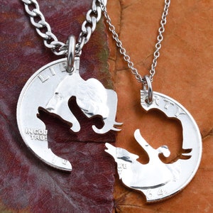 May include: Two silver necklaces with matching pendants. Each pendant is a silver coin with a silhouette of an elephant cut out. The elephants are facing each other and appear to be kissing.