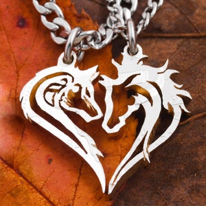 May include: A silver necklace with a heart-shaped pendant featuring two animal silhouettes, a wolf and a horse, facing each other.