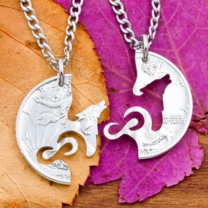 May include: Two silver necklaces with wolf pendants. The pendants are cut out of a silver coin and fit together to form a complete wolf. The necklaces are displayed on a background of fall leaves.