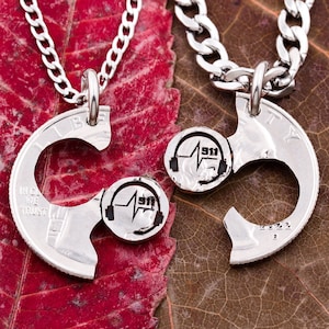 May include: Two silver necklaces with a heart-shaped pendant made from a cut US quarter coin. The coin has the words "In God We Trust" and "Liberty" engraved on it. The heart is split in half, with one half featuring a stylized image of a stethoscope and the number "911" on it. The other half of the heart is missing, suggesting it is a matching pair.