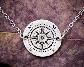 Puede incluir: Un collar de plata con un colgante de brújula. La brújula tiene un diseño detallado con una estrella en el centro y las direcciones NW, NE, SW y SE alrededor del borde.