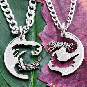 Op de afbeelding: Twee zilveren kettingen met bijpassende hangers. De hangers zijn uitgesneden uit Amerikaanse kwartjes en hebben een wolfontwerp. Het wolfontwerp is verdeeld over de twee hangers, zodat ze samen een complete wolf vormen.