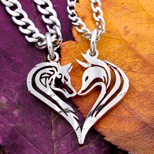 May include: Two silver necklaces with fox head pendants, intertwined and forming a heart shape. The necklaces are on a background of purple and orange leaves.