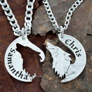 May include: Two silver-coloured, matching pendant necklaces. Each pendant is a half-moon shape with a wolf design. One pendant has the name "Samantha" engraved, the other has "Chris". Both pendants are connected to a silver chain.
