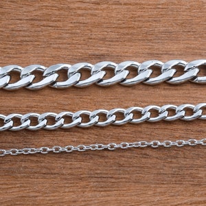 May include: Three silver chains of different thicknesses and styles on a brown wooden surface.