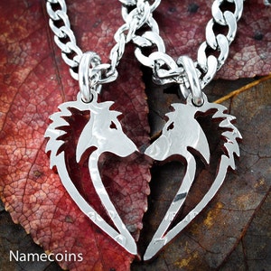 May include: Two silver necklaces with wolf head pendants that form a heart shape when joined together. The necklaces are on a red and brown background.