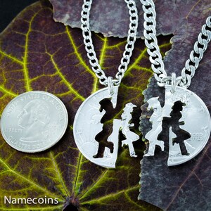 May include: Two silver necklaces with matching pendants. The pendants are cut out of silver coins and feature a couple holding hands. The necklaces are on a green leaf background.