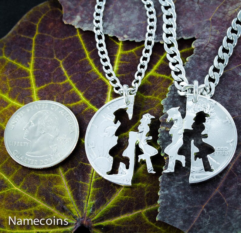 May include: Two silver necklaces with matching pendants. The pendants are cut out of silver coins and feature a couple holding hands. The necklaces are on a green leaf background.