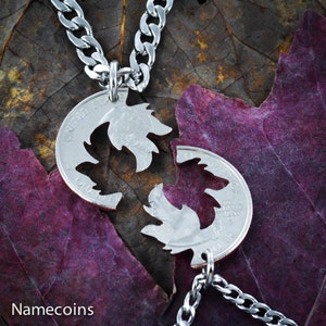 May include: A silver chain necklace with two silver quarter coins that are cut in half and fit together to form a heart shape. The coins are on a purple leaf background.