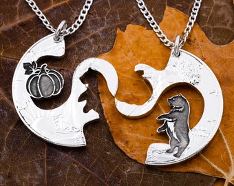 Puede incluir: Dos collares de plata con un diseño de rompecabezas. Un collar presenta una calabaza y el otro un oso. Los collares están sobre un fondo de hoja marrón.