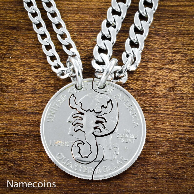 May include: Two silver necklaces with a matching pair of silver quarter dollar coins. The coins are cut in half and feature a scorpion design. The text "UNITED STATES OF AMERICA", "LIBERTY", "IN GOD WE TRUST", and "QUARTER DOLLAR" is visible on the coins.