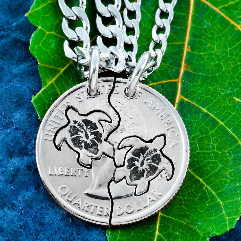 May include: A silver necklace with two matching pendants, each featuring a turtle and a hibiscus flower, cut from a US quarter dollar coin. The pendants are connected by a silver chain.