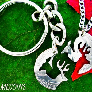 May include: Two silver quarter dollar coins with a deer cut out of them. The coins are connected by a silver chain and a silver key ring. The coins are on a green leaf and a red leaf.