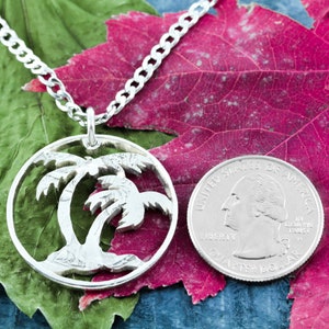 May include: A silver necklace with a palm tree pendant made from a cut-out US quarter coin. The coin features the profile of George Washington and the words "United States of America", "Liberty", and "Quarter Dollar".