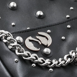 May include: A black leather bag with silver studs and a silver chain strap. A silver coin with a wolf design is attached to the bag.